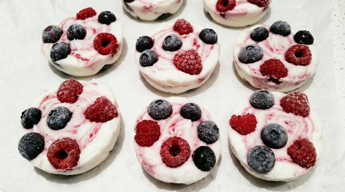 frozen yogurt clusters with blueberries and raspberries on white parchment paper